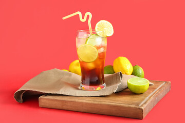 Wooden board with glass of tasty Long Island iced tea and citrus fruits on red background