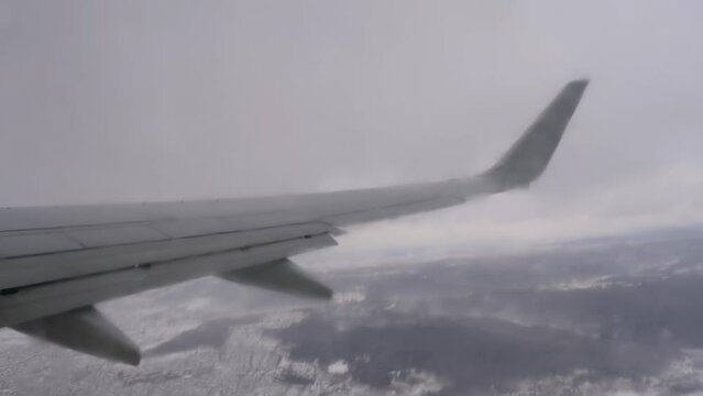 View of snowy landscape under the plane wing through plane porthole. White snow covered space and bright blue sky. Plane engine and winglet as seen from cabin
