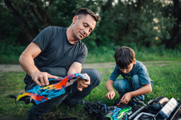Young son and his father fixing their toy cars next to a dirt road