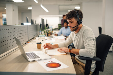 Portrait of a young man working on a laptop in call center and using a headset