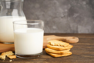 Milk in glass and jug with cookie on wooden table on a grey background, close-up.
