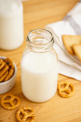 Milk in jug with cookie on wooden table and light background, vertically, close-up.