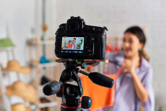 selective focus of digital camera near asian stylist showing bespoke clothes in private atelier