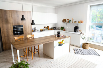 Interior of modern kitchen with white furniture and wooden island table