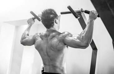 Young strong man bodybuilder doing pulling up on the bar in a modern gym