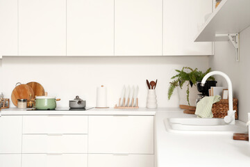 Fototapeta na wymiar White counters with electric stove, sink and utensils in modern kitchen