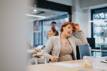 Gorgeous, pregnant businesswoman working on her individual tasks at work while sitting at working desk.