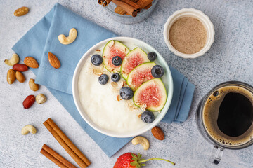 Bowl of tasty semolina porridge with berries, figs and cup of coffee on white background