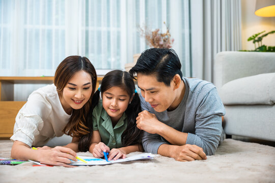 Smiling Father, Mother and daughter drawing together on paper at home, Asian family lying on floor painting with child daughter in living room, Happy family activity enjoy, learning draw art picture