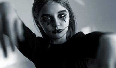 Little girl with spooky Halloween makeup looking at camera like zombie. Creepy kid's portrait in...