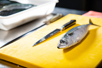 Pescado fresco en una  tabla de cortar con cuchillo y afilador en una cocina de un restaurante