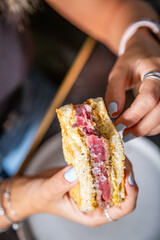 Sandwich de tartar de carne de lomo alto de ternera con salsa en pan tostado, tomado por manos de chica con las uñas pipntadas en la mesa de un restaurante 