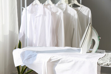 Electric iron with white shirt on board in room