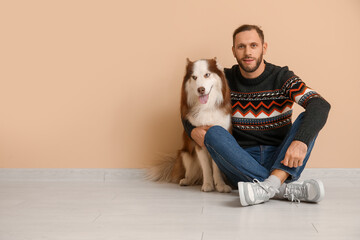 Handsome young man with cute Husky dog near beige wall