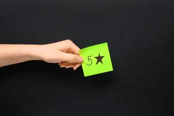 Woman holding paper with five stars rating on dark background. Customer experience concept