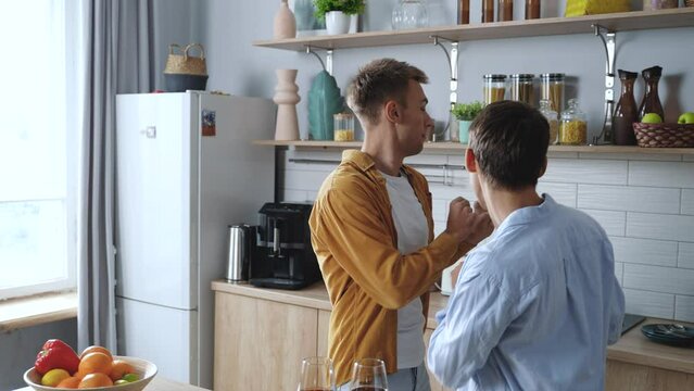 Carefree young adult gay men celebrating weekend, celebrating move day, while funny dancing in a cozy kitchen. Happy couple having fun while preparing food. High quality 4k footage