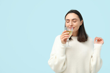 Beautiful young woman with glass of white wine on blue background