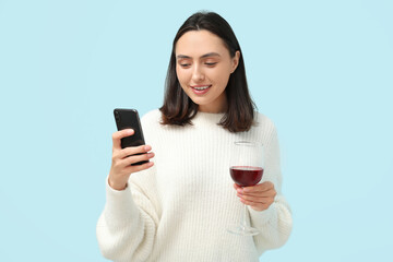 Beautiful young woman with glass of red wine and mobile phone on blue background