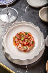 tartar de salmón sobre un plato blanco cuenco con brotes decorativos, salsa de cítricos, aceite de oliva virgen extra, en una mesa de restaurante de marmol negro con servilleta blanca