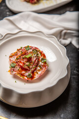 tartar de salmón fresco crudo sobre un plato blanco cuenco con brotes decorativos, salsa de cítricos, aceite de oliva virgen extra, en una mesa de restaurante de marmol negro con servilleta blanca
