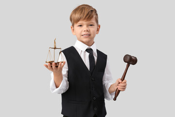 Cute little judge with gavel and justice scales on light background. Opposite Day celebration