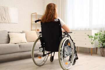 Young redhead woman in wheelchair at home, back view