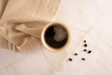 Coffee mug in a marbled stone background with beige napkin and coffee beans in aerial top view