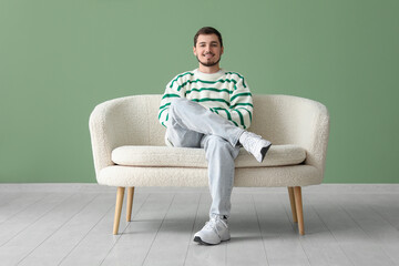 Fototapeta na wymiar Handsome young man sitting on sofa near green wall