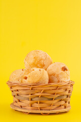 Brazilian cheese bread inside a wooden basket in a clean yellow background in front top view