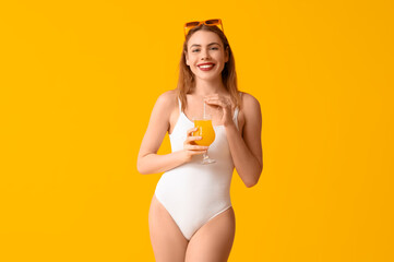 Pretty young woman in tank swimsuit and with cocktail on yellow background - obrazy, fototapety, plakaty