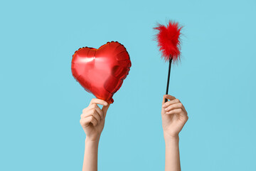 Female hands with heart shaped balloon and feather stick from sex shop on blue background....