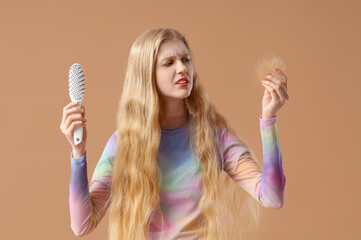 Upset young woman with hair loss problem and brush on beige background