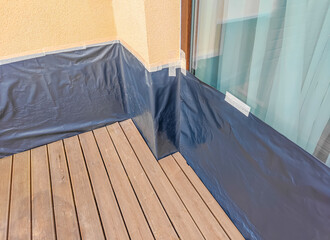 Wooden brown terrace prepared for oiling and painting with walls and windows covered with film. Cleaned decking