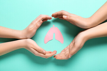 Hands of woman and child with paper lungs on turquoise background