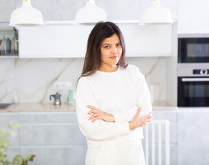 Smiling young brunette in white casual clothes standing in cozy light home kitchen interior..