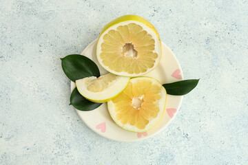 Plate with cut fresh pomelo fruit and leaves on white background