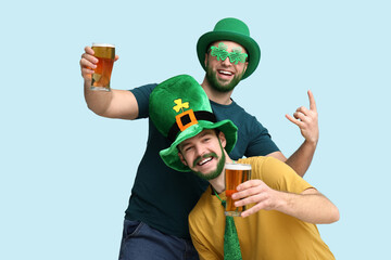Happy young men in leprechaun hats with green beards holding glasses of beer on blue background....