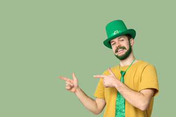 Young man in leprechaun hat with green beard pointing at something on green background. St....