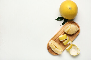 Wooden board with pieces of fresh pomelo fruit and leaves on white background