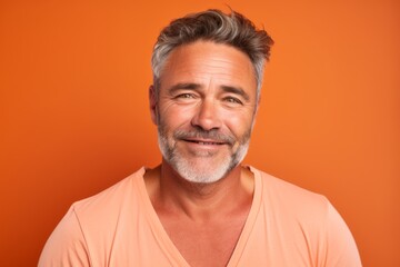 Obraz premium Portrait of happy mature man with grey hair and beard on orange background.