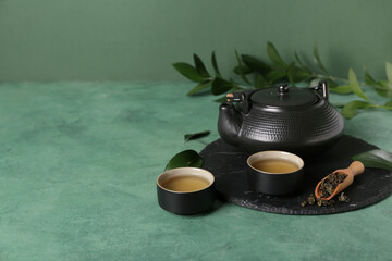 Teapot with cups, scoop of dry tea and leaves on green grunge background