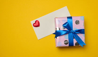 Box tied with a blue ribbon and small hearts on a yellow background, top view