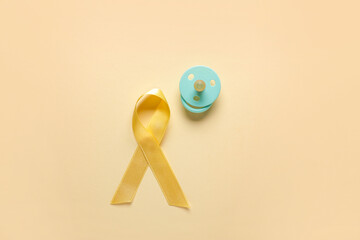 Golden ribbon with pacifiers on yellow background. Childhood cancer awareness concept