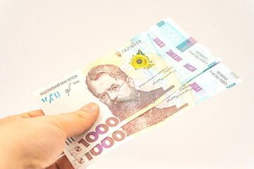 Concept of Ukrainian cash money. Cash payment in Ukraine. A man's hand pays with Ukrainian money. 1000 hryvnia in hand isolated on a white background. Banknote with the maximum Ukrainian denomination
