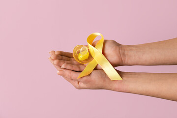 Hands with golden ribbon and pacifier on pink background. Childhood cancer awareness concept