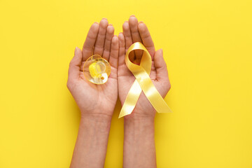 Hands with golden ribbon and pacifier on yellow background. Childhood cancer awareness concept