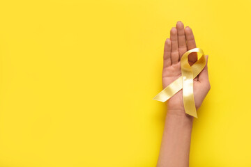 Hand with golden ribbon on yellow background. Childhood cancer awareness concept