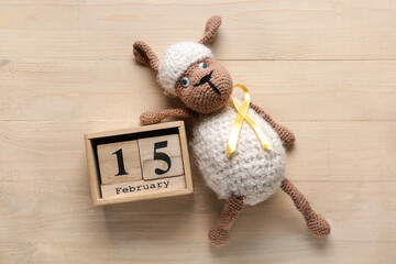 Toy sheep with golden ribbon and calendar on light wooden background. Childhood cancer awareness...