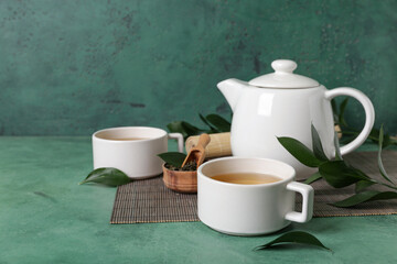 Bamboo mat with teapot, cups of tea and leaves on green grunge background
