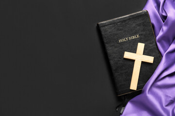 Wooden cross with Bible and purple cloth on black background. Good Friday concept